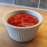 Close-up of bright red homemade cocktail sauce recipe served in a small white fluted ramekin.