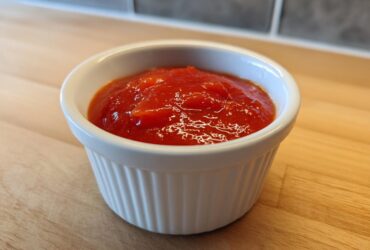 Close-up of bright red homemade cocktail sauce recipe served in a small white fluted ramekin.