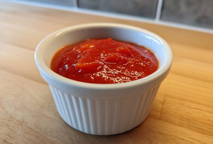 Close-up of bright red homemade cocktail sauce recipe served in a small white fluted ramekin.