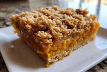 A close-up shot of a thick, square slice of pumpkin crisp bar with a gooey orange filling and crumbly topping.