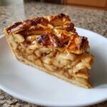 A close-up of a thick slice of apple pies showing layered filling and a golden lattice crust.