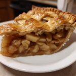 Close-up of a slice of apple pies showing thick, chunky apple filling and a golden, flaky lattice crust.