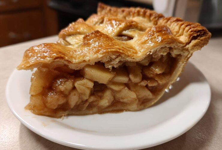 Close-up of a slice of apple pies showing thick, chunky apple filling and a golden, flaky lattice crust.