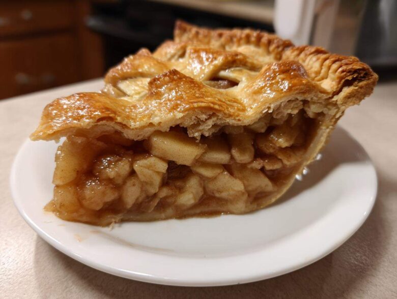 Close-up of a slice of apple pies showing thick, chunky apple filling and a golden, flaky lattice crust.