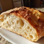 Cross-section of artisan bread showing an open, airy crumb structure and a deeply browned, crisp crust.