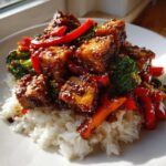 Close-up of an Asian inspired Tofu Dish With Rice and Vegetables, featuring glazed tofu cubes, broccoli, and red peppers.