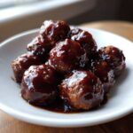 Close-up of several glossy, saucy Asian Meatballs Crockpot served in a small white bowl.
