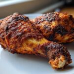 Close-up of two crispy, richly seasoned Baked Chicken Legs resting on a clean white plate.