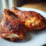 Two juicy, richly seasoned Baked Chicken Legs with crispy, dark brown skin resting on a light blue plate.