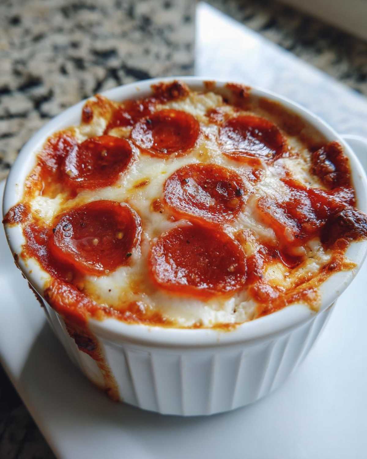 Close-up of a baked cottage cheese pizza bowl topped with melted cheese and pepperoni slices.