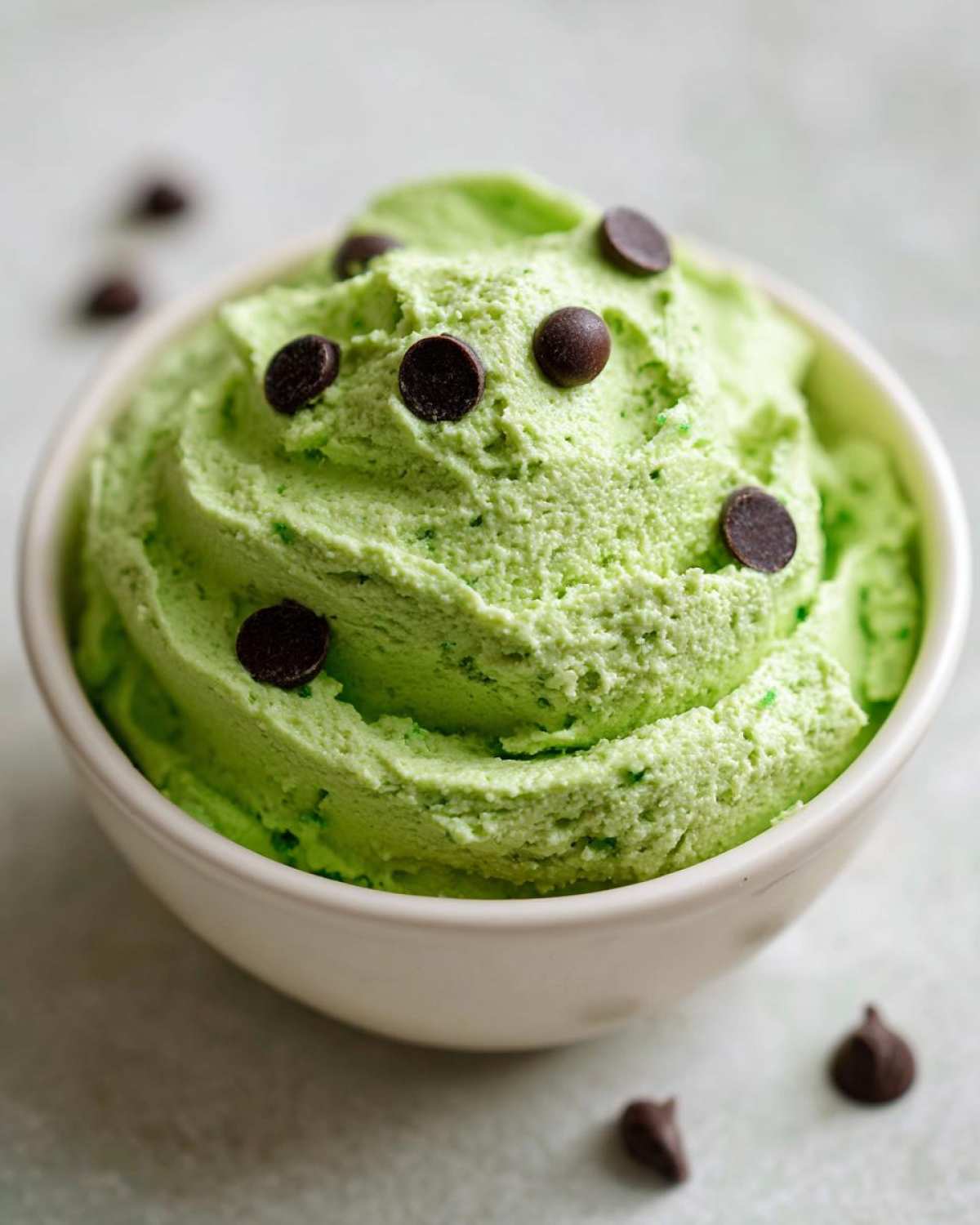 Close-up of a bowl of bright green Grinch dip, swirled and topped with dark chocolate chips.