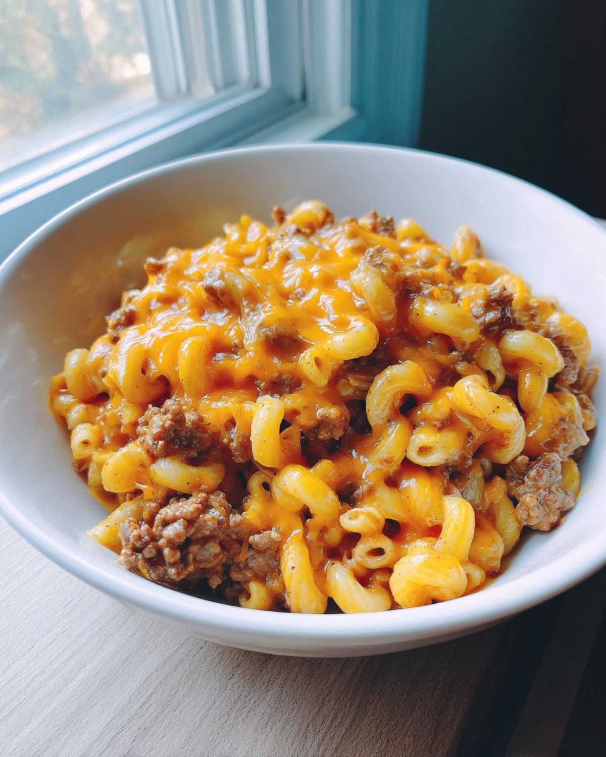 Close-up of a white bowl filled with cheesy taco pasta featuring elbow macaroni and seasoned ground beef.