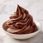 A perfect swirl of rich, dark chocolate buttercream frosting piped into a small white bowl.