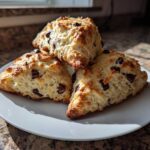 Three freshly baked chocolate chip scones, golden brown and studded with dark chocolate chunks, stacked on a white plate.