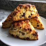 Close-up of three freshly baked, golden brown chocolate chip scones stacked on a white plate.