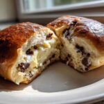 Close-up of a freshly baked chocolate chip vanilla custard brioche cut in half, showing the creamy filling and chocolate chips.