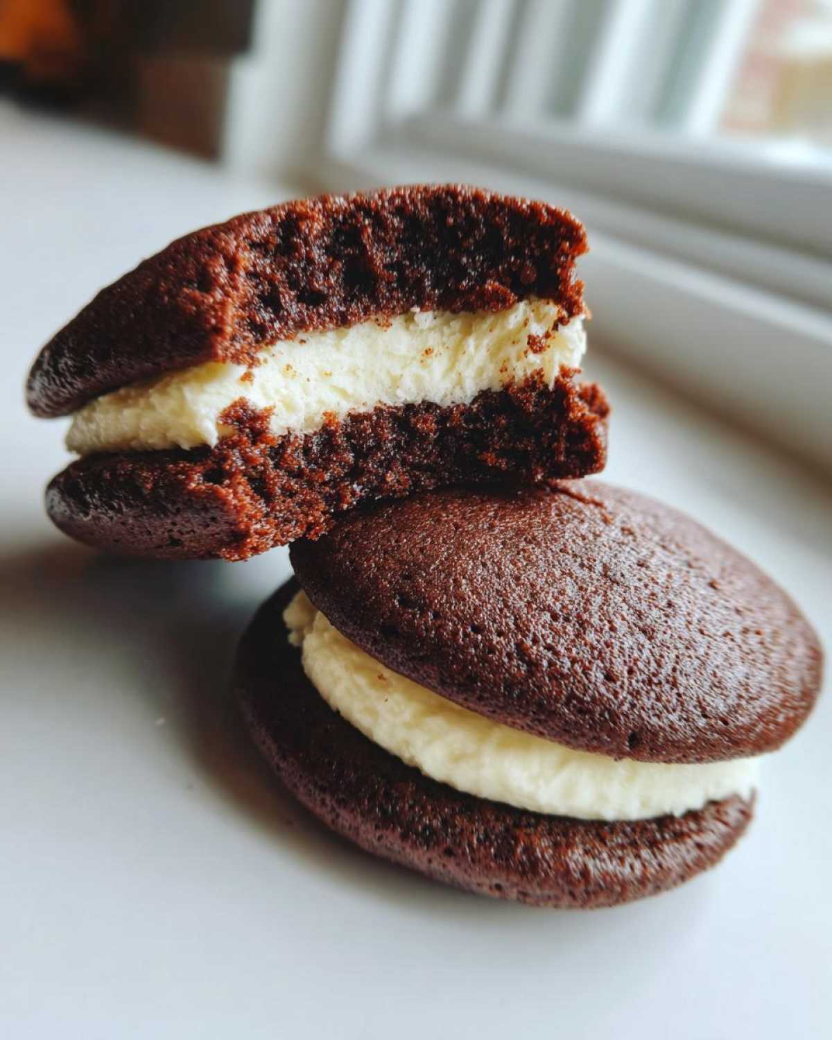 Two chocolate whoopie pies stacked, one cut in half revealing the fluffy white cream filling. Perfect for amazing 11-minute whoopie pies.