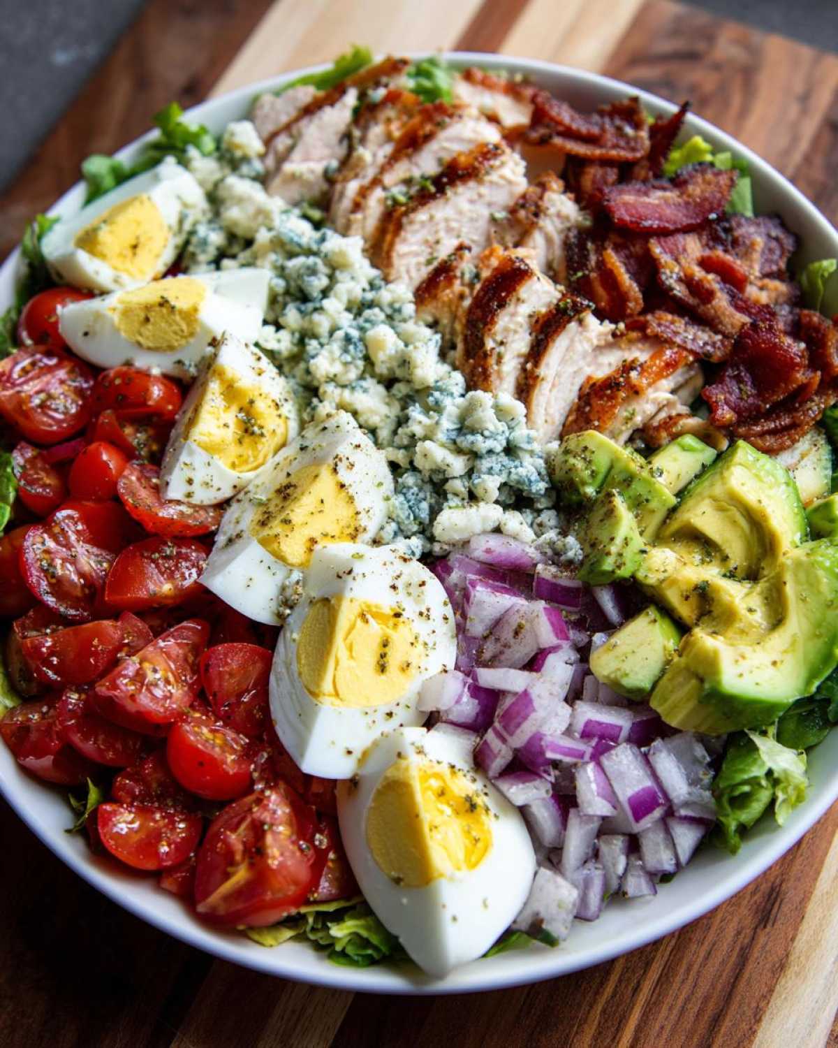 Overhead view of a vibrant cobb salad bowl featuring sliced chicken, bacon, avocado, eggs, and blue cheese.