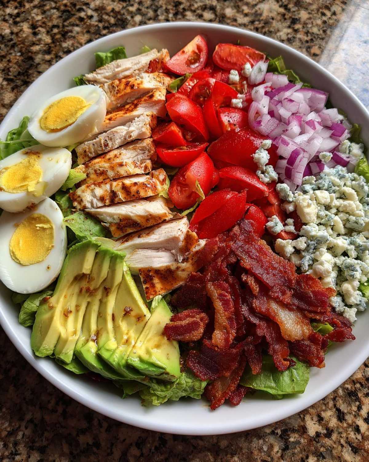 Overhead view of a vibrant cobb salad featuring grilled chicken, avocado, bacon, eggs, tomatoes, and blue cheese.