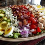 A beautifully arranged plate featuring all the classic ingredients for a cobb salad, including avocado, blue cheese, bacon, chicken, and eggs.