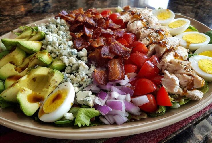 A beautifully arranged plate featuring all the classic ingredients for a cobb salad, including avocado, blue cheese, bacon, chicken, and eggs.