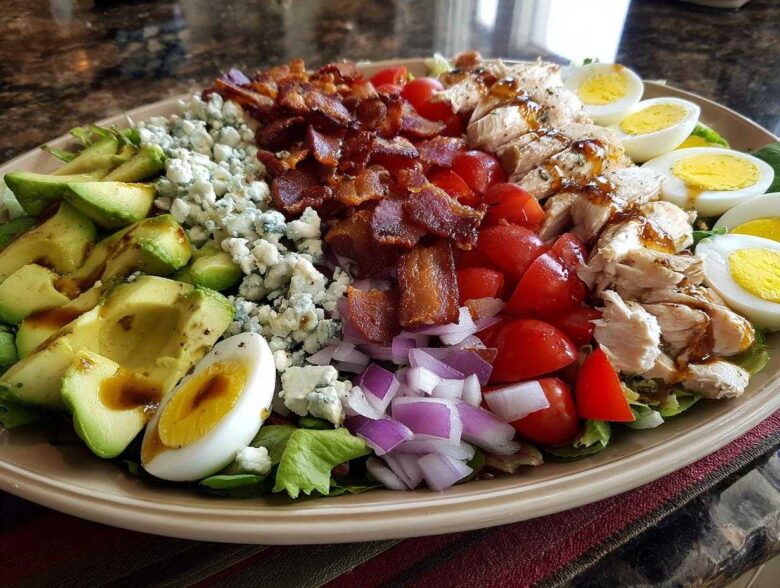 A beautifully arranged plate featuring all the classic ingredients for a cobb salad, including avocado, blue cheese, bacon, chicken, and eggs.