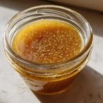 Overhead close-up of homemade Copycat Apple Cider Vinaigrette, golden brown with visible spices, stored in a small glass jar.
