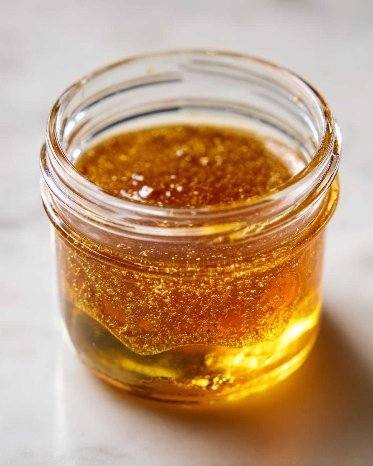 Close-up of golden, emulsified Copycat Apple Cider Vinaigrette dressing in a small glass jar.