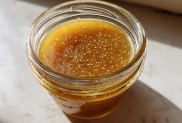 Overhead close-up of homemade Copycat Apple Cider Vinaigrette, golden brown with visible spices, stored in a small glass jar.