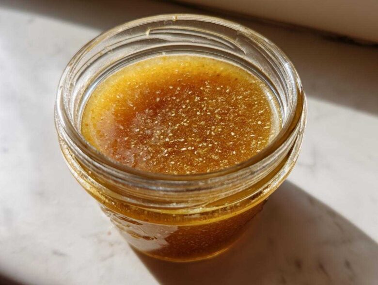 Overhead close-up of homemade Copycat Apple Cider Vinaigrette, golden brown with visible spices, stored in a small glass jar.