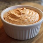 A close-up of creamy, orange-hued Copycat Classic Burger Spread Sauce swirled in a small white ramekin.