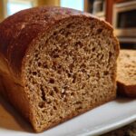 Close-up of a freshly baked loaf of Copycat Dark Brown Honey Wheat Bread, showing the dark crust and open, moist crumb texture.