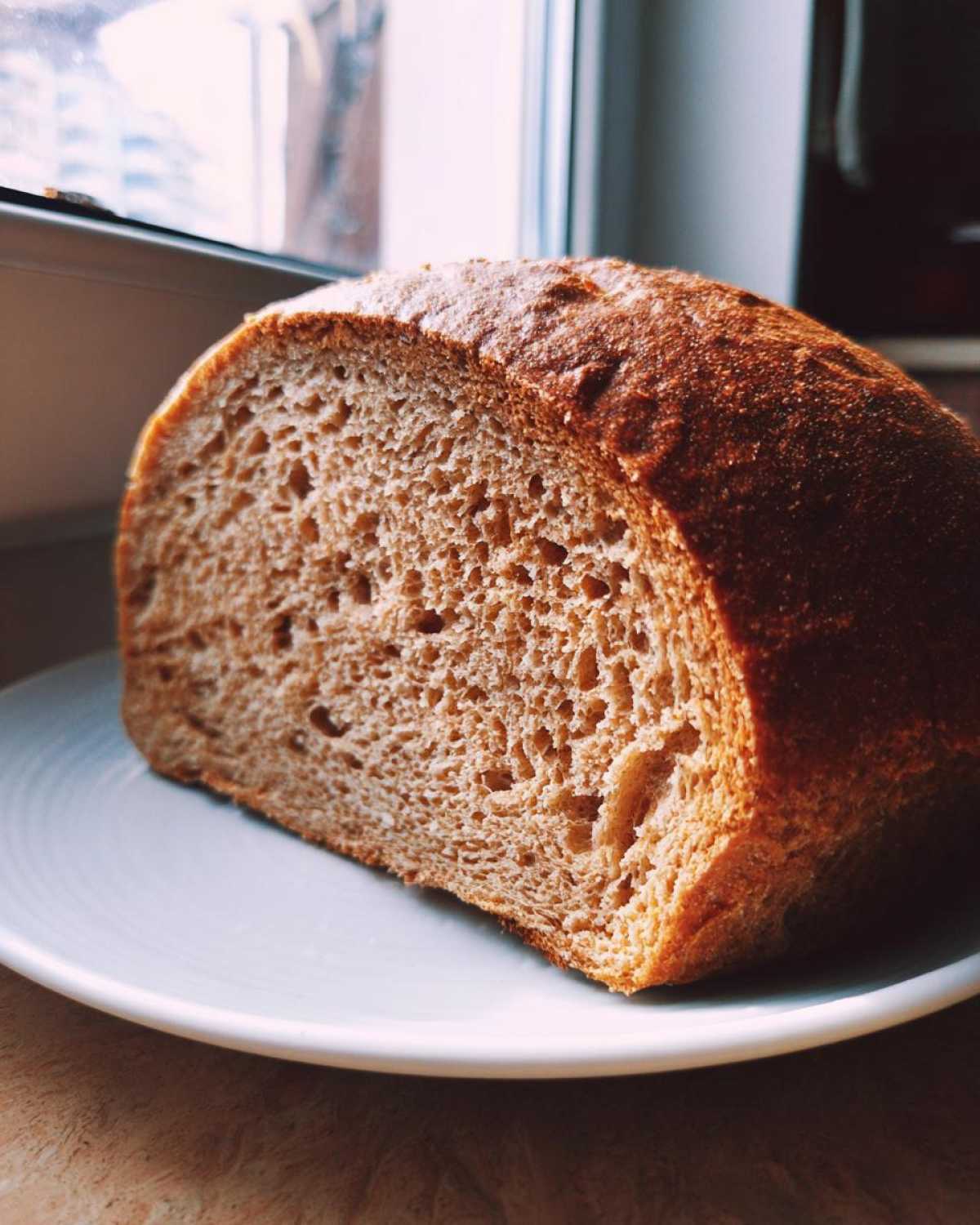 Cross-section of a freshly baked loaf of Copycat Dark Brown Honey Wheat Bread resting on a light blue plate.