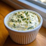 A close-up of creamy Copycat Pizza Garlic Parmesan Dip Sauce topped with fresh parsley and lemon zest in a white ramekin.