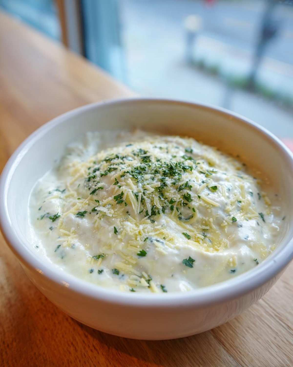 Close-up of a creamy Copycat Pizza Garlic Parmesan Dip Sauce topped with shredded cheese and fresh parsley.