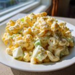 A close-up of creamy Amish macaroni salad featuring elbow pasta, chopped celery, and hard-boiled egg pieces on a white plate.