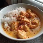 Close-up of creamy cajun chicken pieces served next to fluffy white rice, topped with red pepper flakes.