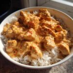 A white bowl filled with white rice topped with creamy, seasoned chunks of cajun chicken.