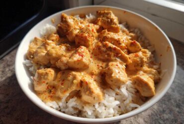 A white bowl filled with white rice topped with creamy, seasoned chunks of cajun chicken.