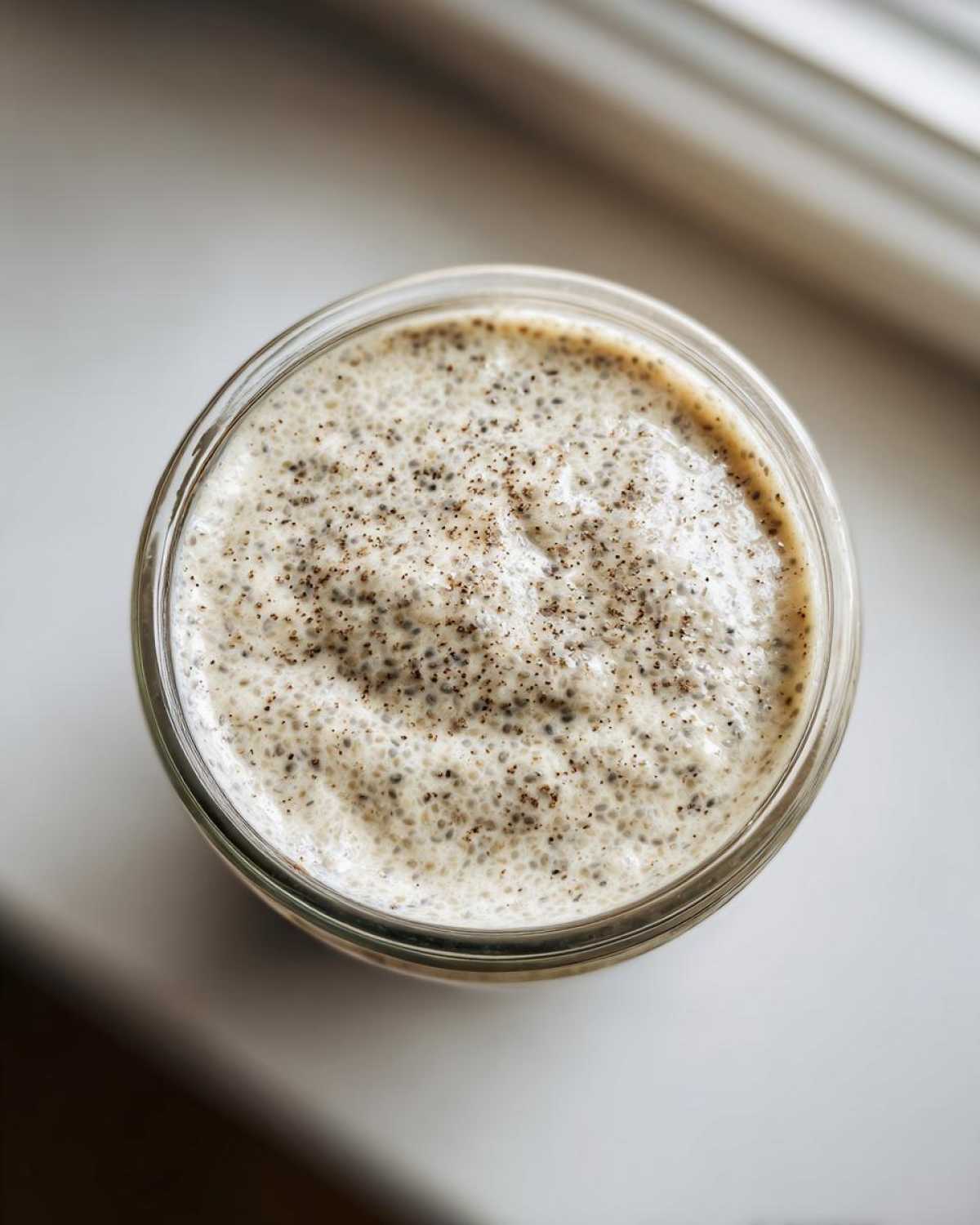 Overhead view of creamy chia seed pudding texture inside a glass jar, showing soaked chia seeds.