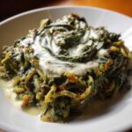 Close-up of a serving of persian noodle soup featuring noodles and greens topped with a creamy sauce.