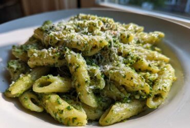 Close-up of a bowl filled with creamy pesto pasta (penne) topped generously with grated Parmesan cheese.