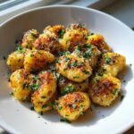 A white bowl filled with golden, crispy air fryer gnocchi topped with grated parmesan and fresh chopped parsley.