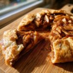 A close-up view of a slice of rustic apple galette with caramelized cinnamon apples on a wooden board.