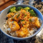A close-up of an easy Bang Bang Chicken bowl featuring crispy chicken tossed in spicy sauce over white rice with steamed broccoli florets.