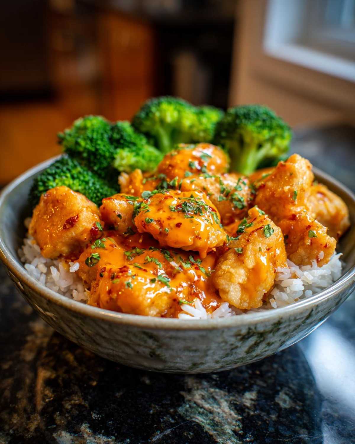 A close-up of an easy Bang Bang Chicken bowl featuring crispy chicken coated in orange sauce over white rice, served with steamed broccoli.