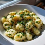 A close-up of tender gnocchi coated in a creamy garlic butter sauce, topped with fresh parsley and grated cheese, ready to eat.