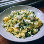 A bowl of Easy One-Pot Creamy Lemon Herb Couscous topped with crumbled feta cheese and fresh herbs.