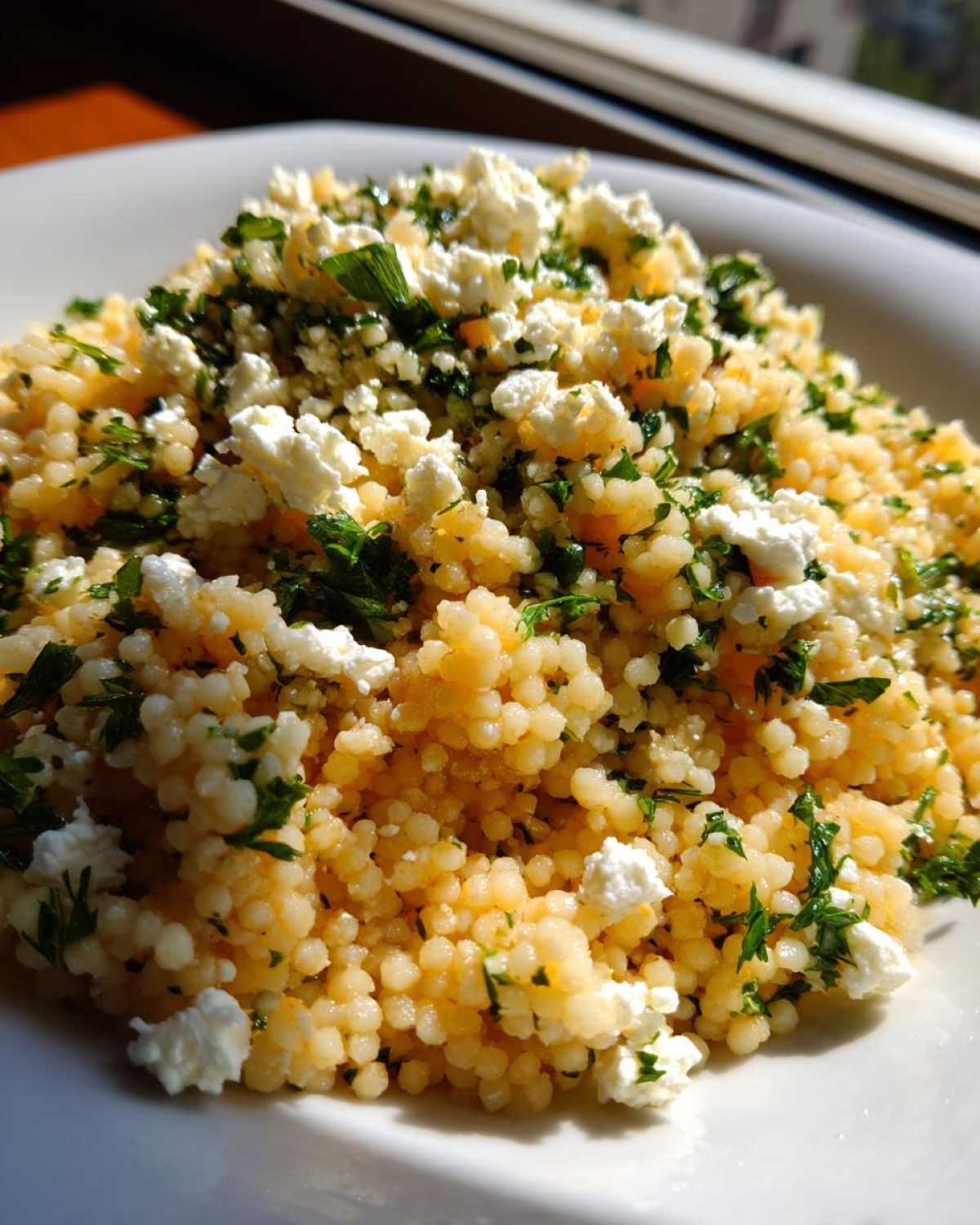 A close-up of fluffy, golden Easy One-Pot Creamy Lemon Herb Couscous topped with crumbled feta cheese and fresh parsley.