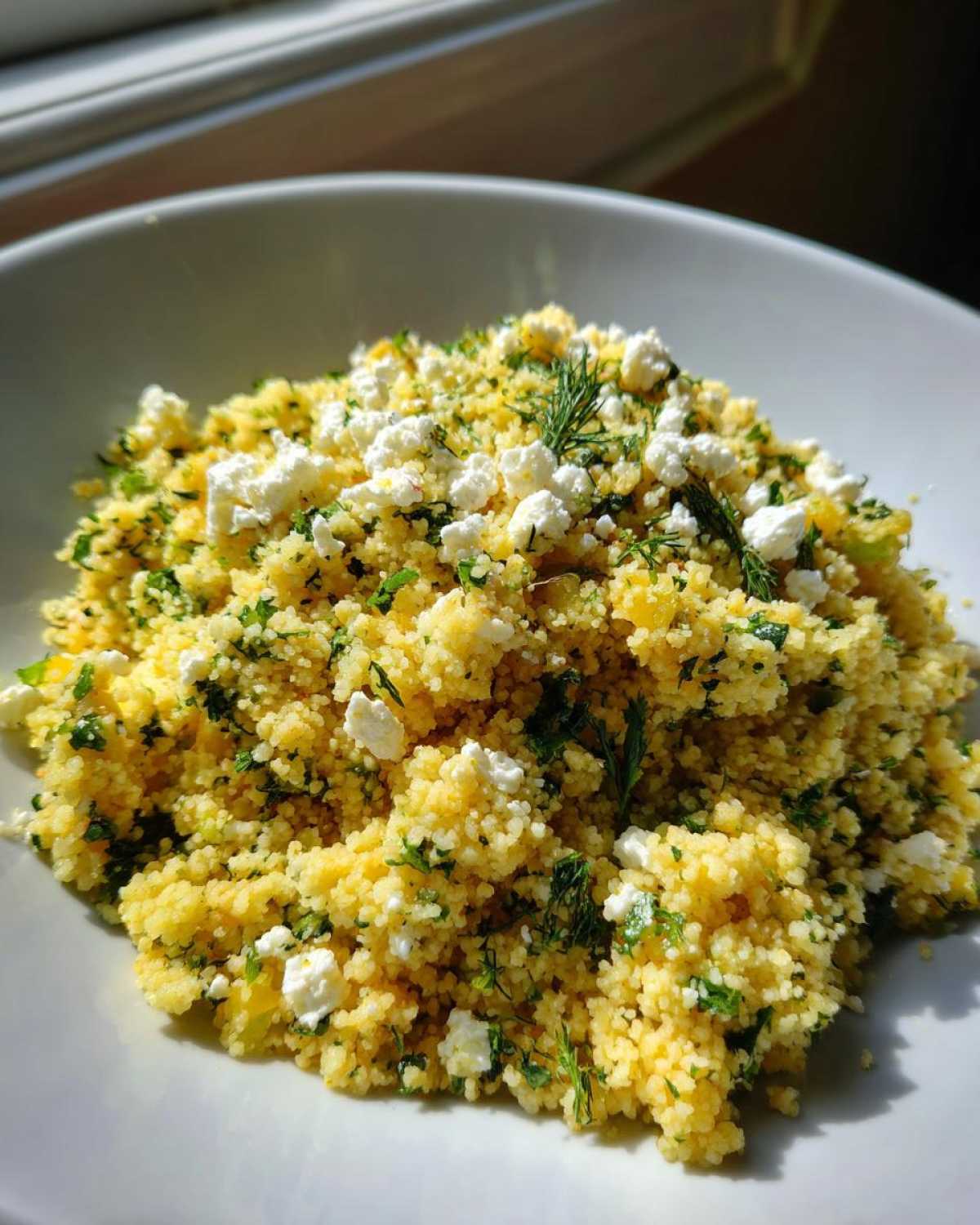 A close-up of Easy One-Pot Creamy Lemon Herb Couscous topped with crumbled feta and fresh dill.
